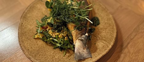 A plate with a fish, greens, and grains.