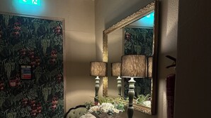 A bathroom with a green chair, a vanity with a mirror, and a floral-patterned wall. - The George Hotel Easingwold (York)