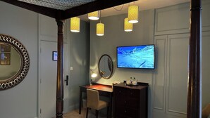 A bedroom with a bed, a desk with a mirror, a television, and a chandelier. - The George Hotel Easingwold (York)