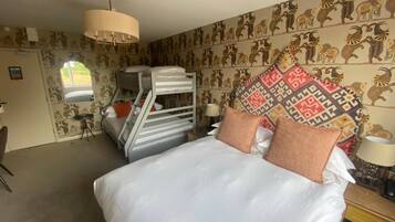 A bedroom with a large bed, patterned wallpaper, a hanging light fixture, and a window.