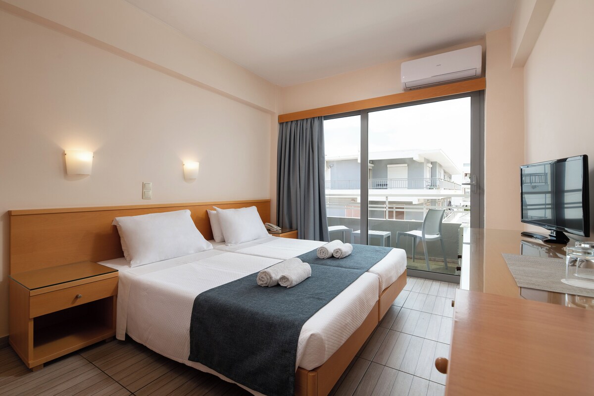 A hotel room with a bed, bedside tables, a TV, and a balcony with a view.
