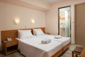 A hotel room with two beds, a nightstand with a phone, a chair, and a bathroom visible through a glass door.
