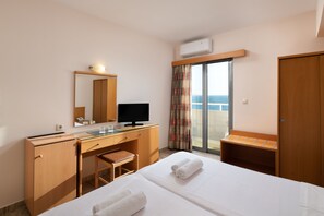 A hotel room with a bed, a desk, a chair, a television, a mirror, and a view of the sea. - Nafsika Hotel (Rhodes)