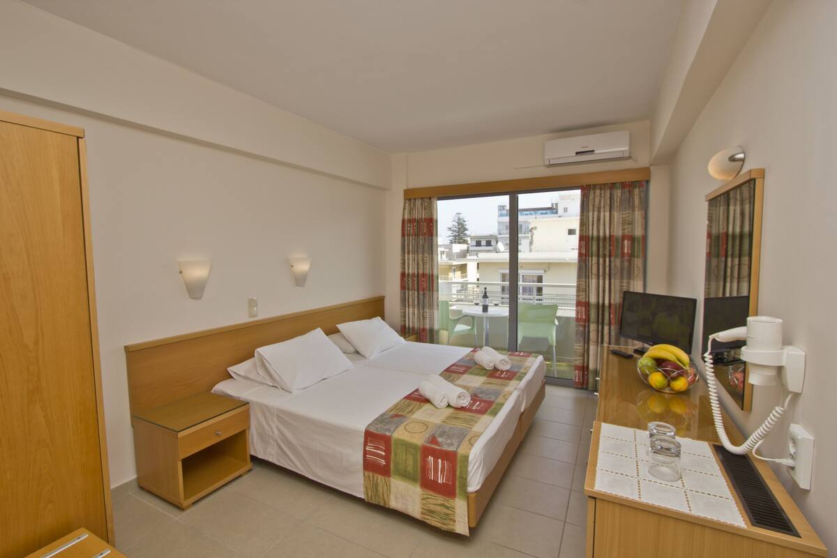 A hotel room with a bed, bedside table, and a desk with a telephone and a glass of water.