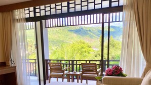 A spacious balcony with a wooden table and two chairs, a sofa, and a view of lush greenery. - Le Murraya Boutique Hotel (Koh Samui)