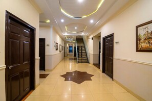 A hotel hallway with a star-patterned floor, dark wooden doors, and a staircase leading to an upper floor. - Hotel One Lalazar Multan (Multan)