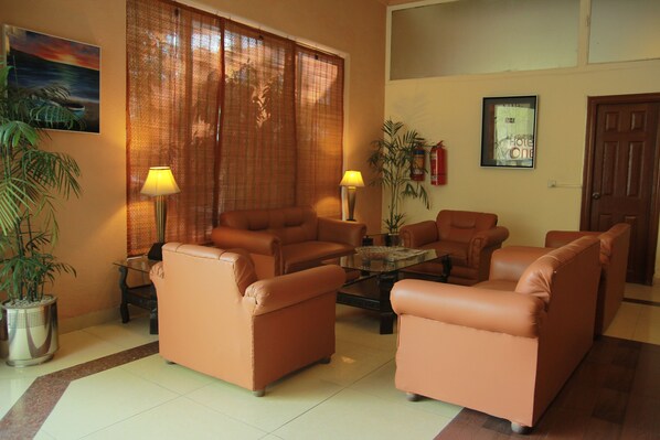A living room with four brown leather sofas arranged around a glass coffee table, two floor lamps, and a potted plant. - Hotel One Lalazar Multan (Multan)