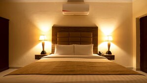 Une chambre d’hôtel avec un grand lit, deux lampes de chevet, une tête de lit en bois et un appareil de climatisation placé au-dessus du lit.