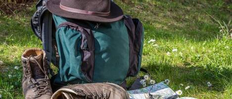 Una mochila verde, un sombrero marrón y un par de botas de senderismo marrones sobre hierba, junto con un mapa y una brújula.