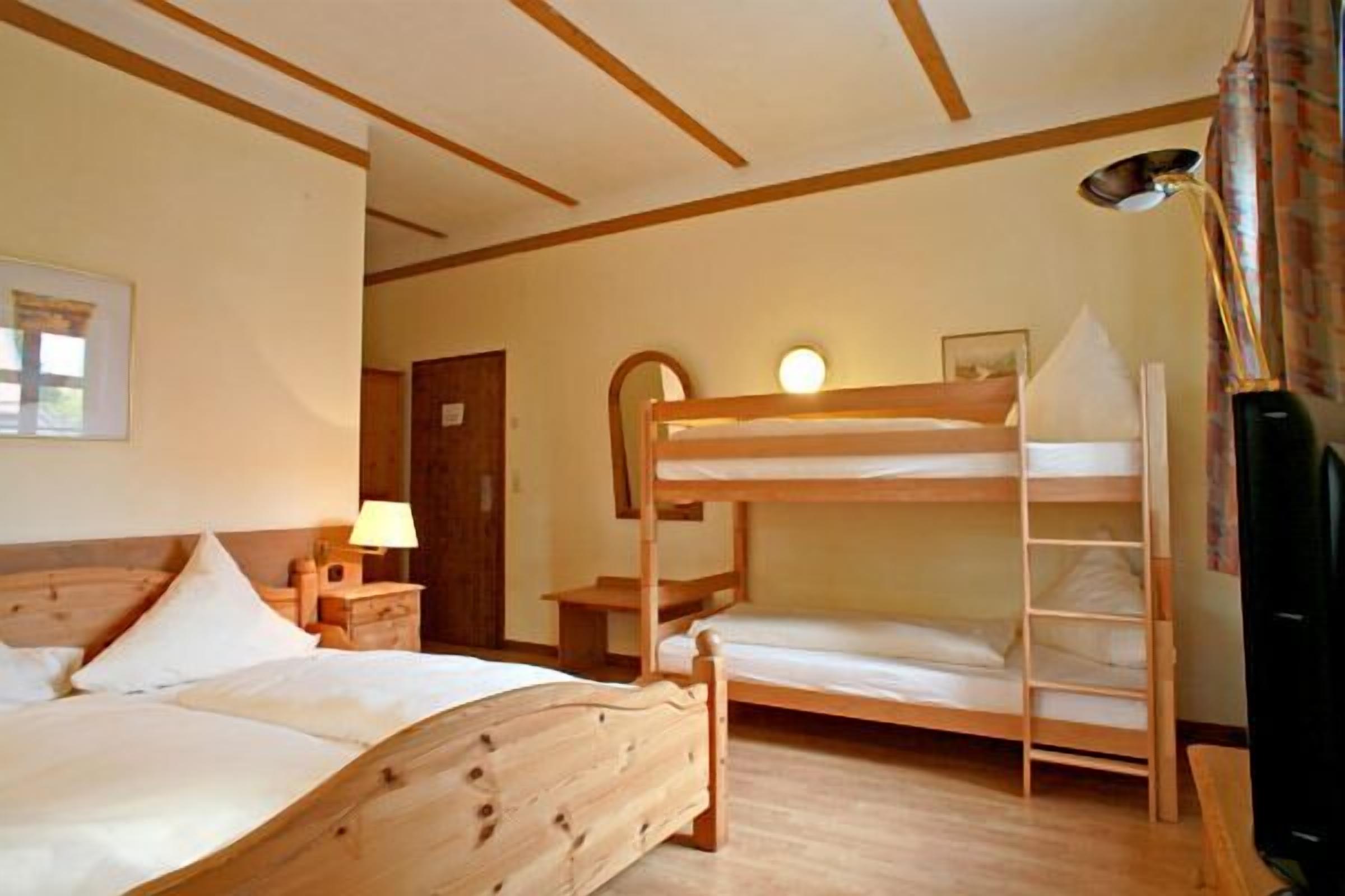 Una habitación con una cama litera de madera, una mesita de noche con lámpara y un escritorio pequeño.