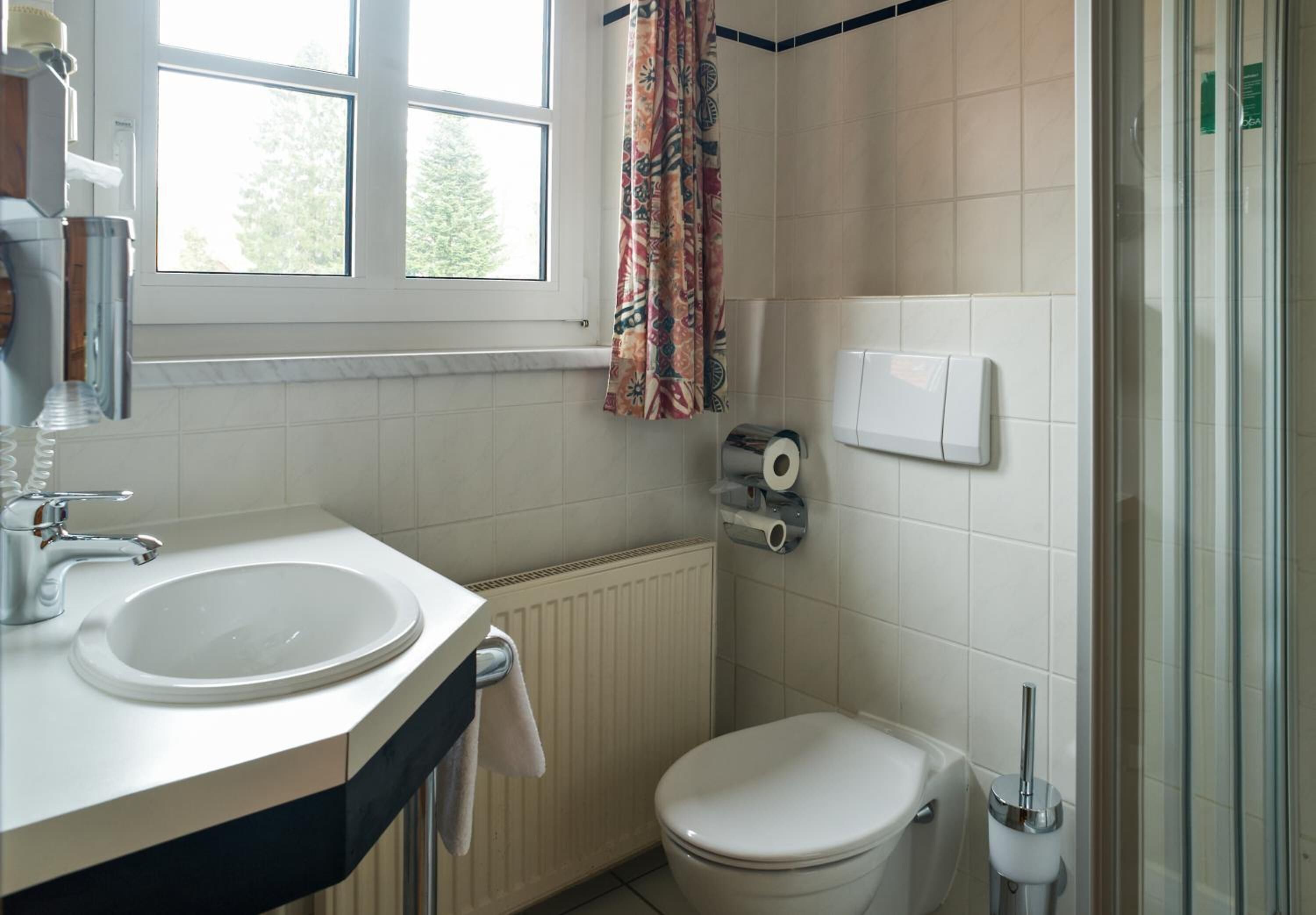 Un baño con lavabo, inodoro, ducha y ventana con cortina.