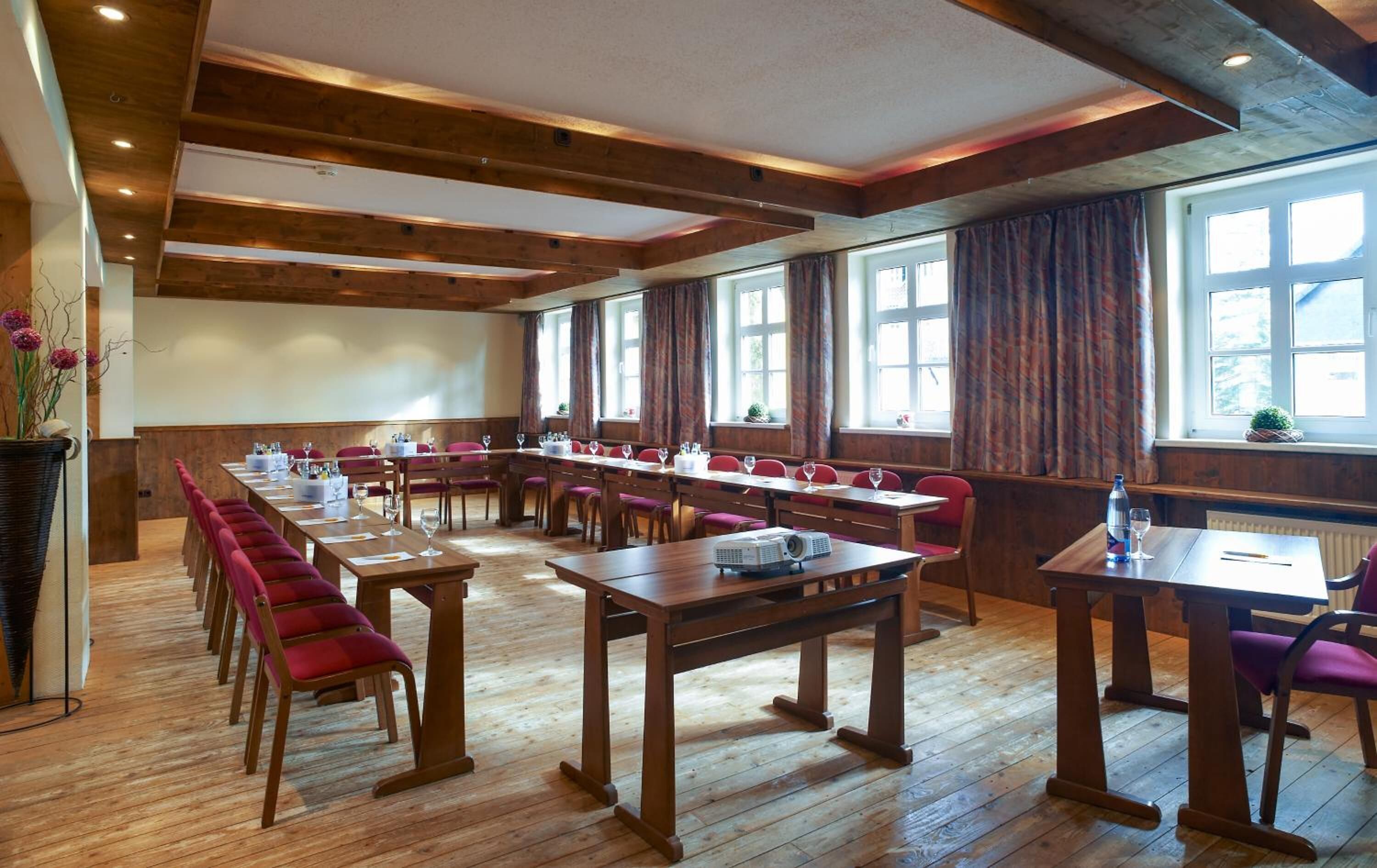 Ein Konferenzraum mit Holztischen und -stühlen, großen Fenstern und einem Projektor auf einem Tisch.