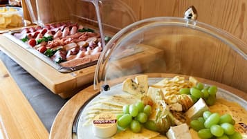A buffet with various cheeses, meats, and grapes.