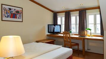 A hotel room with a bed, desk, chair, and a computer.