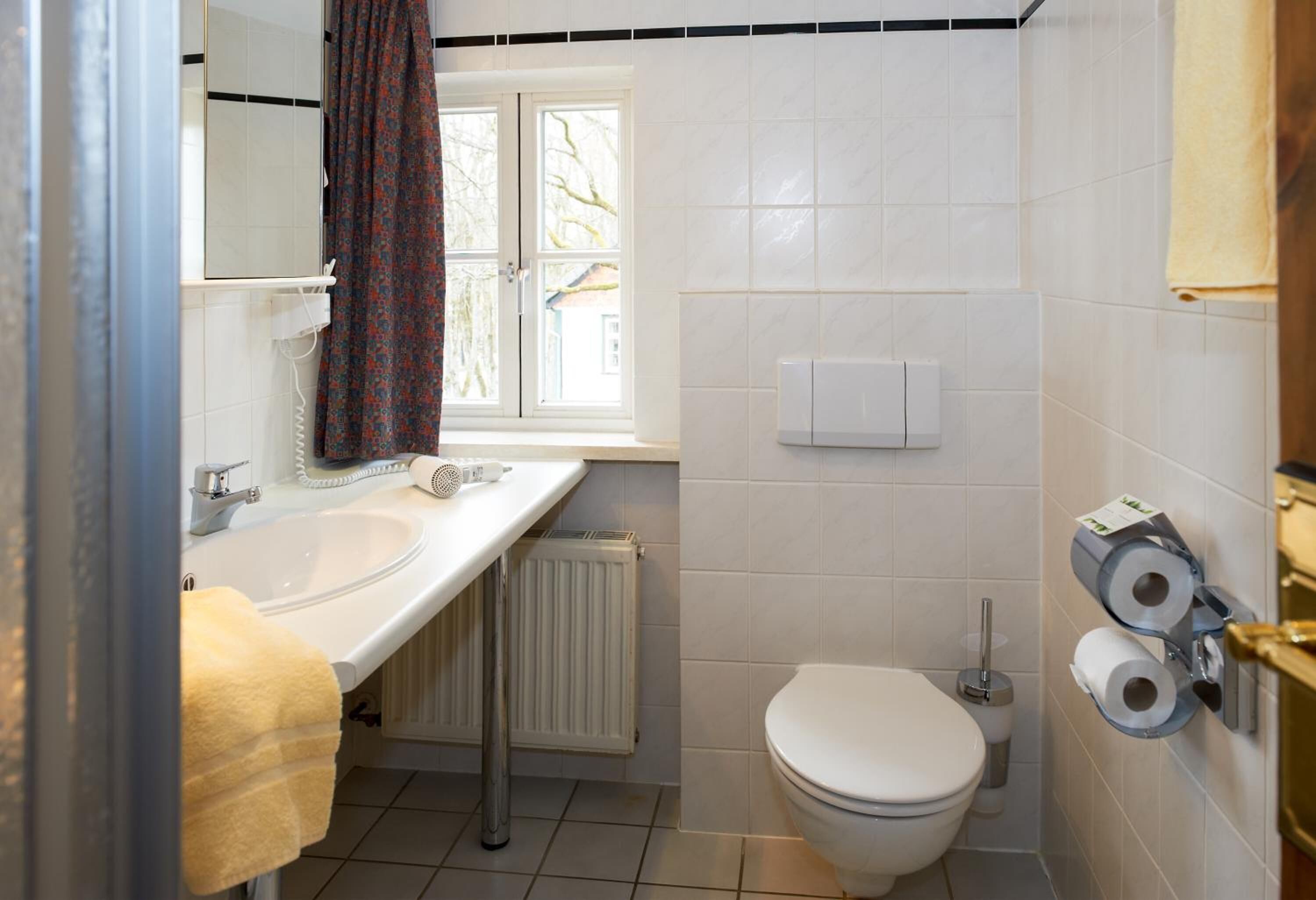 Une salle de bain avec un lavabo blanc, des toilettes et une fenêtre avec un rideau.