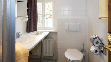 Une salle de bain avec un lavabo blanc, des toilettes et une fenêtre avec un rideau.