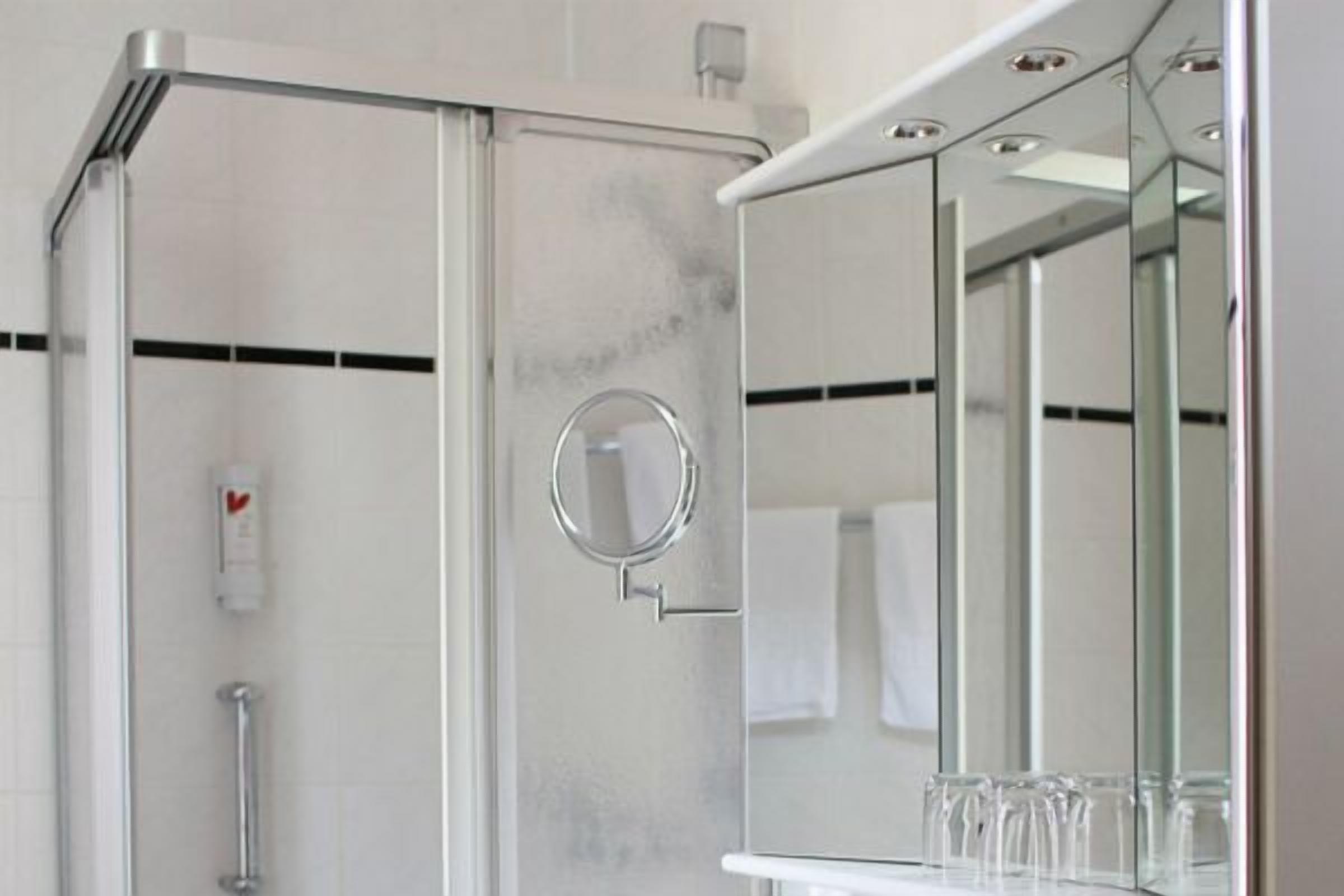 A modern bathroom with a glass shower enclosure, a round mirror, and a glass shelf with toiletries.