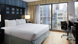 A hotel room with a large bed, a desk with a chair, a window with a city view, and a balcony. - Fairfield Inn & Suites by Marriott New York ManhattanChelsea (New York)