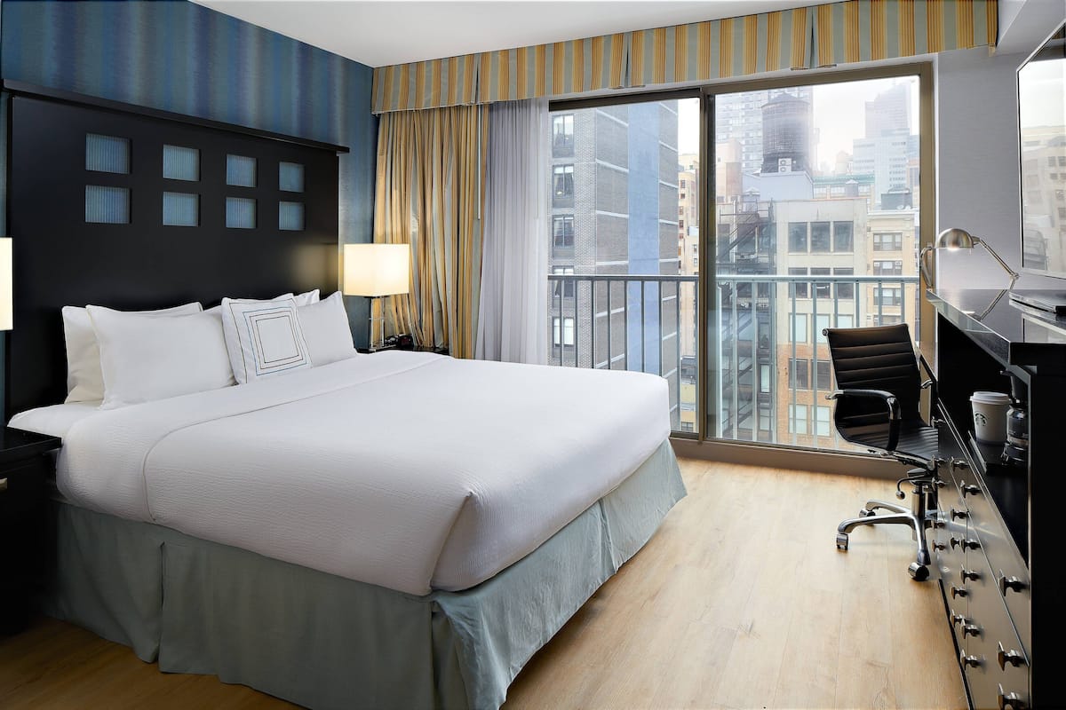 Ein Hotelzimmer mit einem großen Bett, einem Schreibtisch mit Stuhl, einem Fenster mit Stadtblick und einem Balkon.