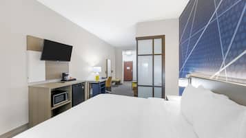 Une chambre d’hôtel équipée d’un lit, d’un bureau, d’un four à micro-ondes, d’une chaise et d’un téléviseur fixé au mur.