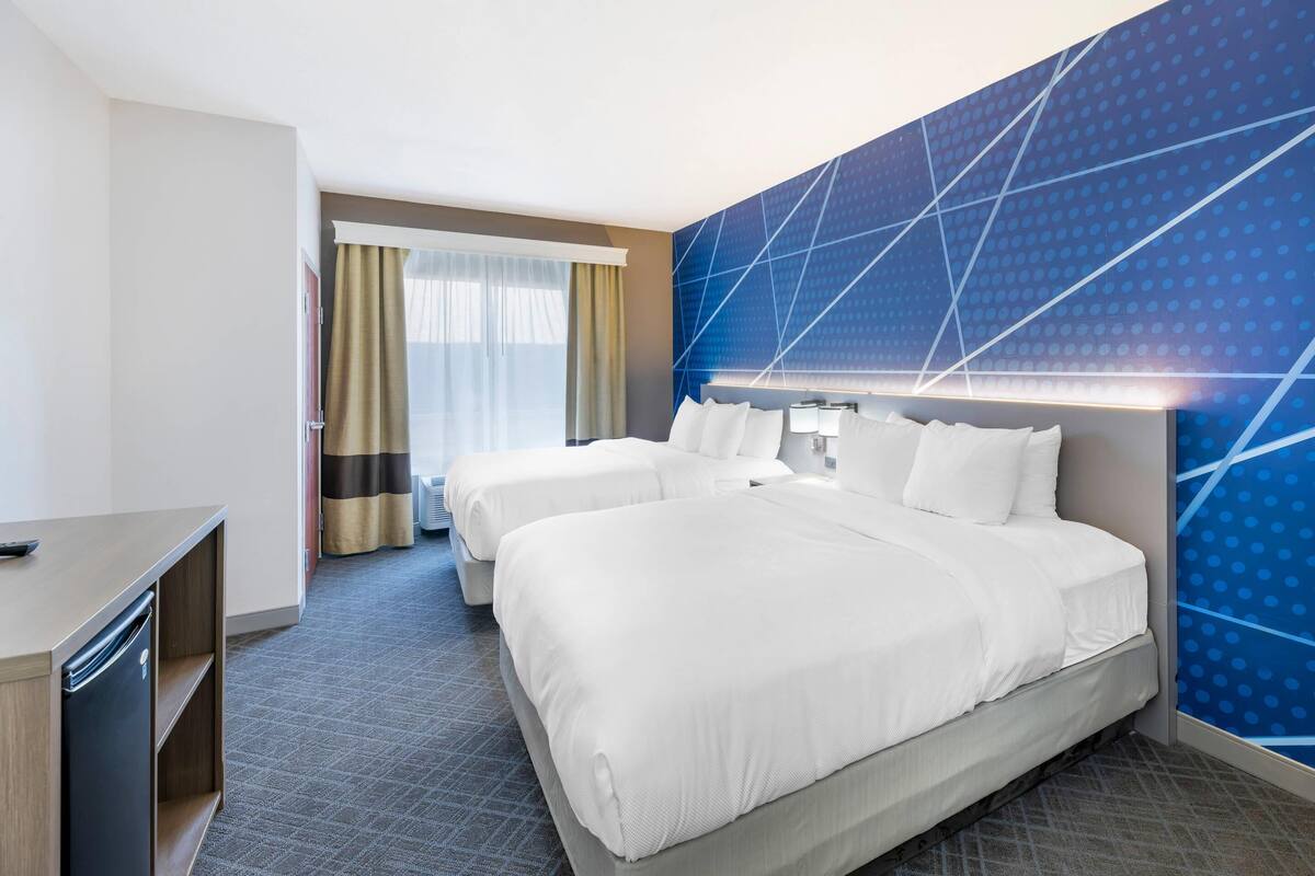A hotel room with two beds, a desk, and a minibar.