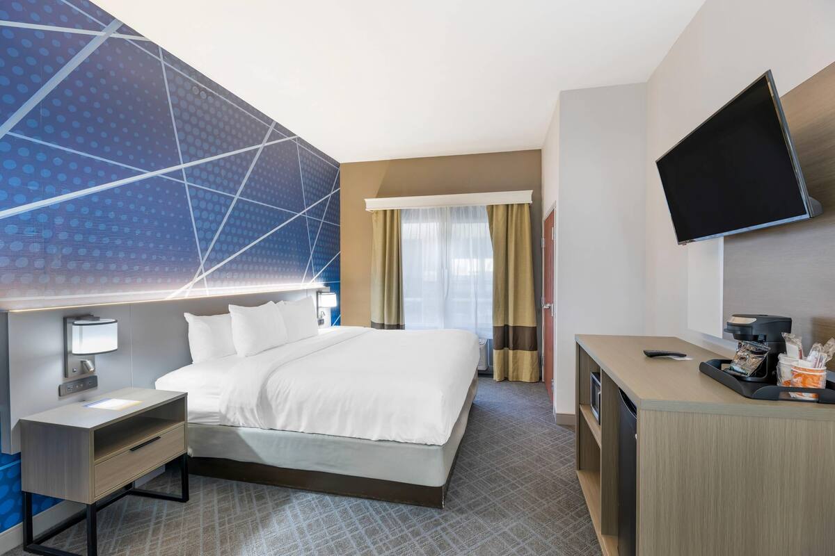 A hotel room with a bed, a desk, a TV, and a large window with curtains.