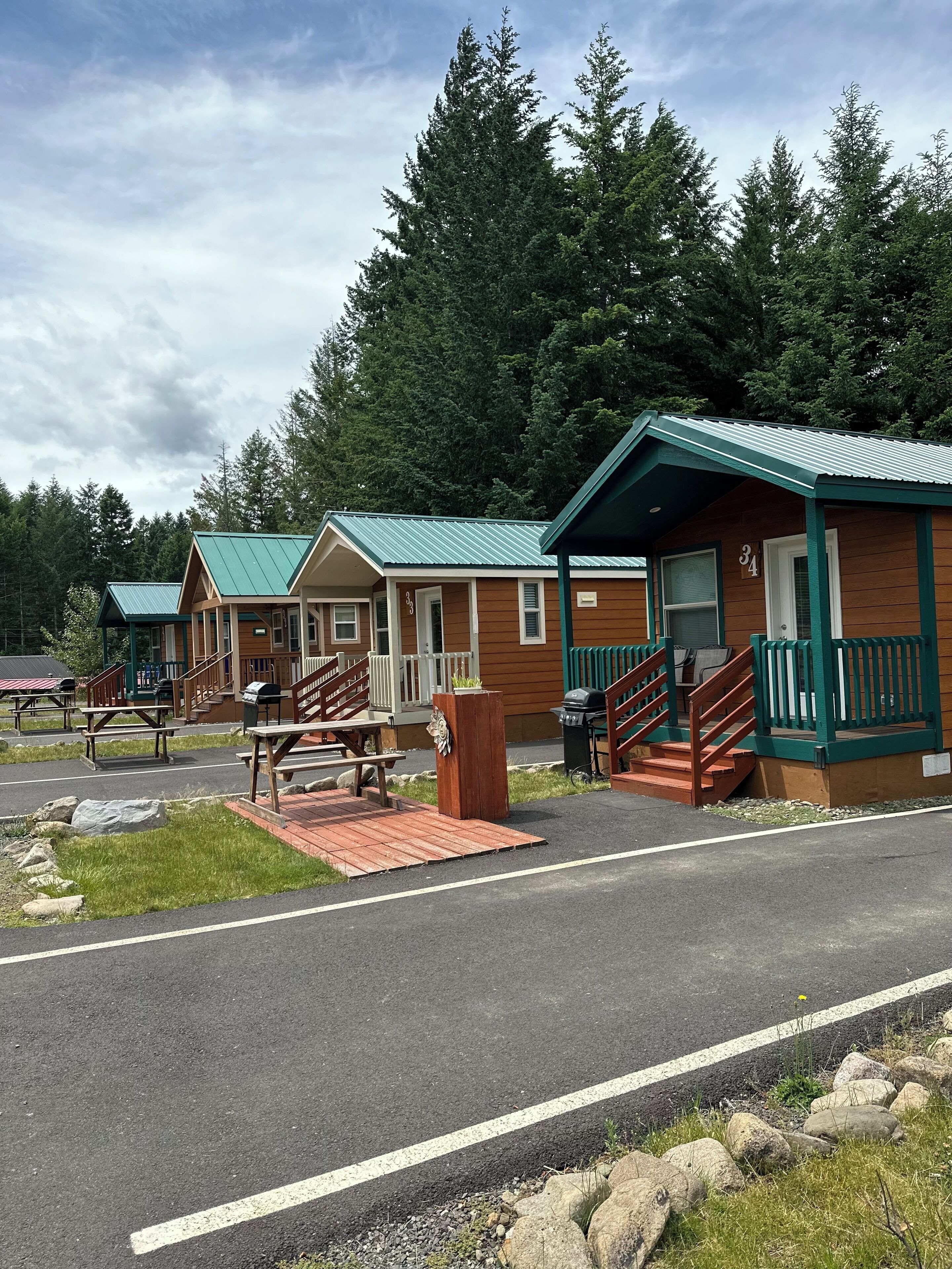 A row of cabins with green roofs, wooden exteriors, and a paved driveway leading to a picnic area.