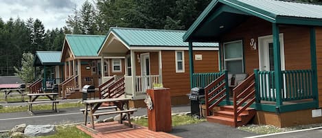 A row of cabins with green roofs, wooden exteriors, and a paved driveway leading to a picnic area.