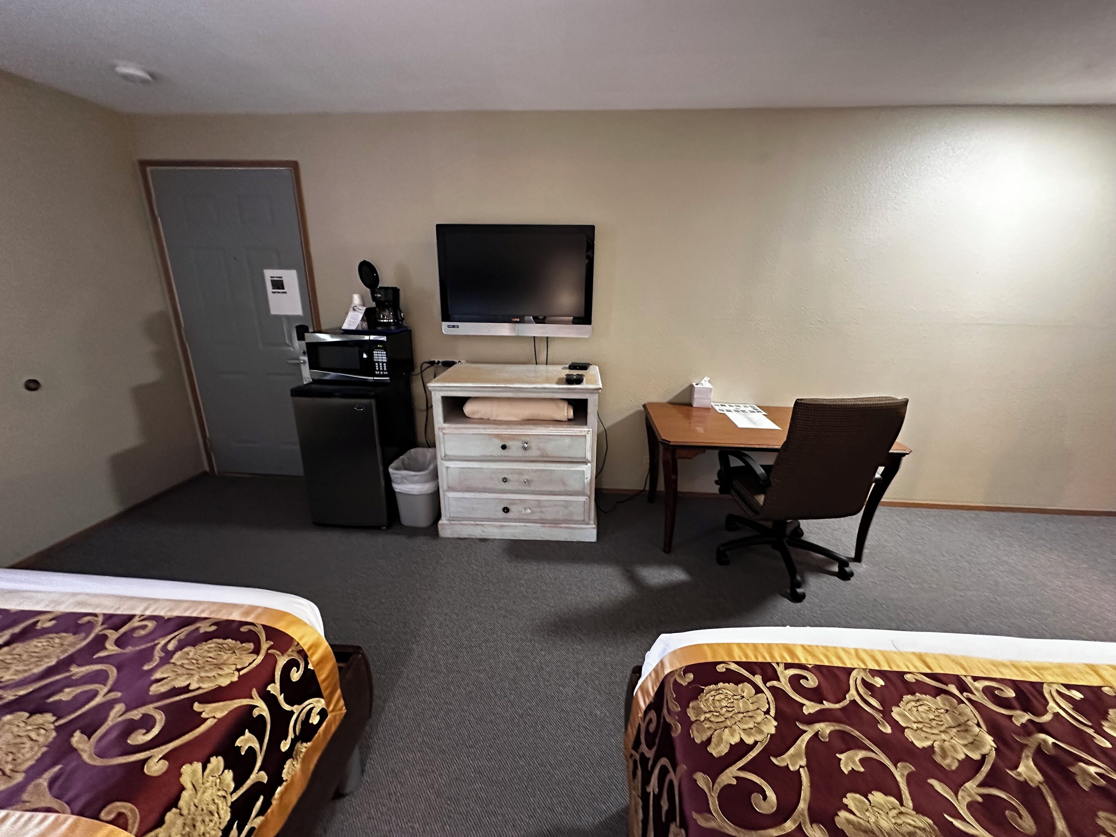 A hotel room with two beds, a desk, a chair, a television, a microwave, and a trash bin.