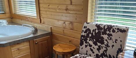 A wooden interior with a large bathtub, a round mirror, and a cow-patterned chair.