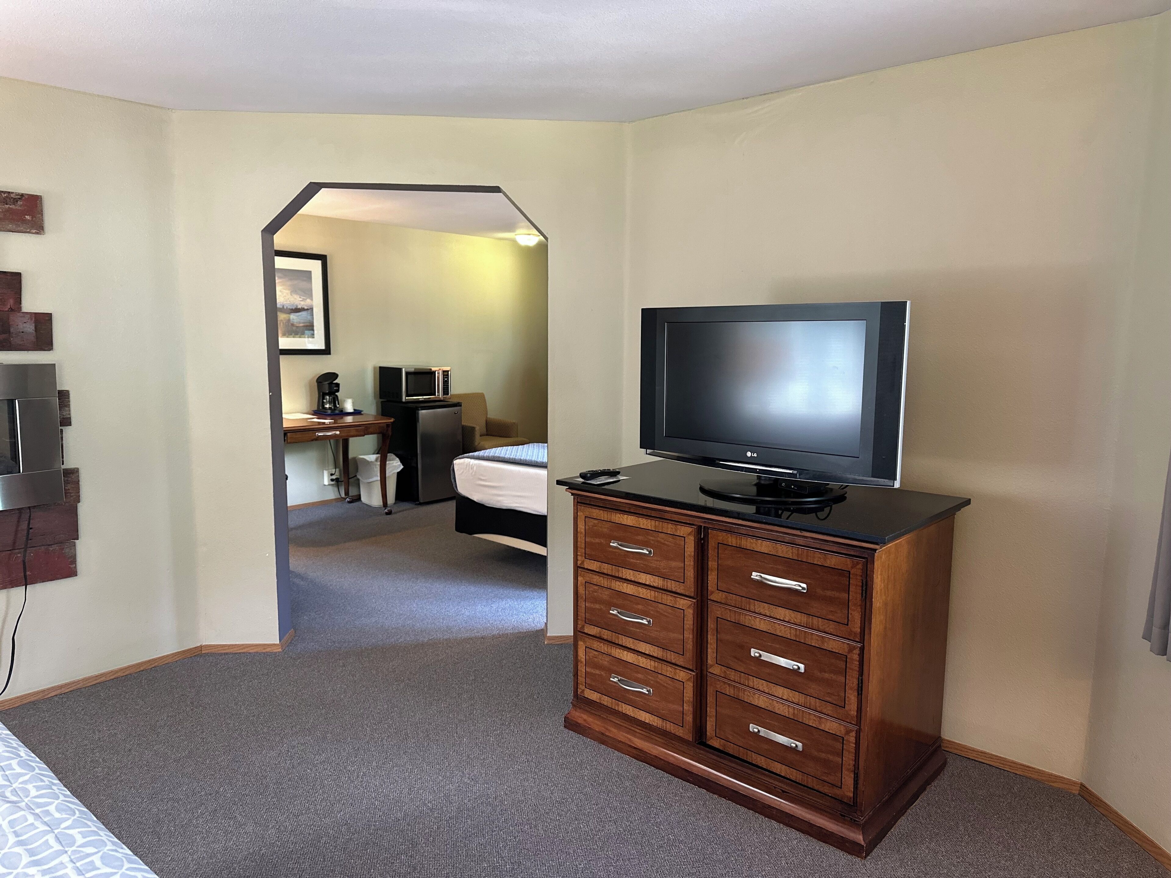 Une chambre d’hôtel avec une commode en bois, un téléviseur posé dessus, un lit recouvert d’une courtepointe à motifs bleus et blancs, et un bureau avec un four à micro-ondes et une machine à café.
