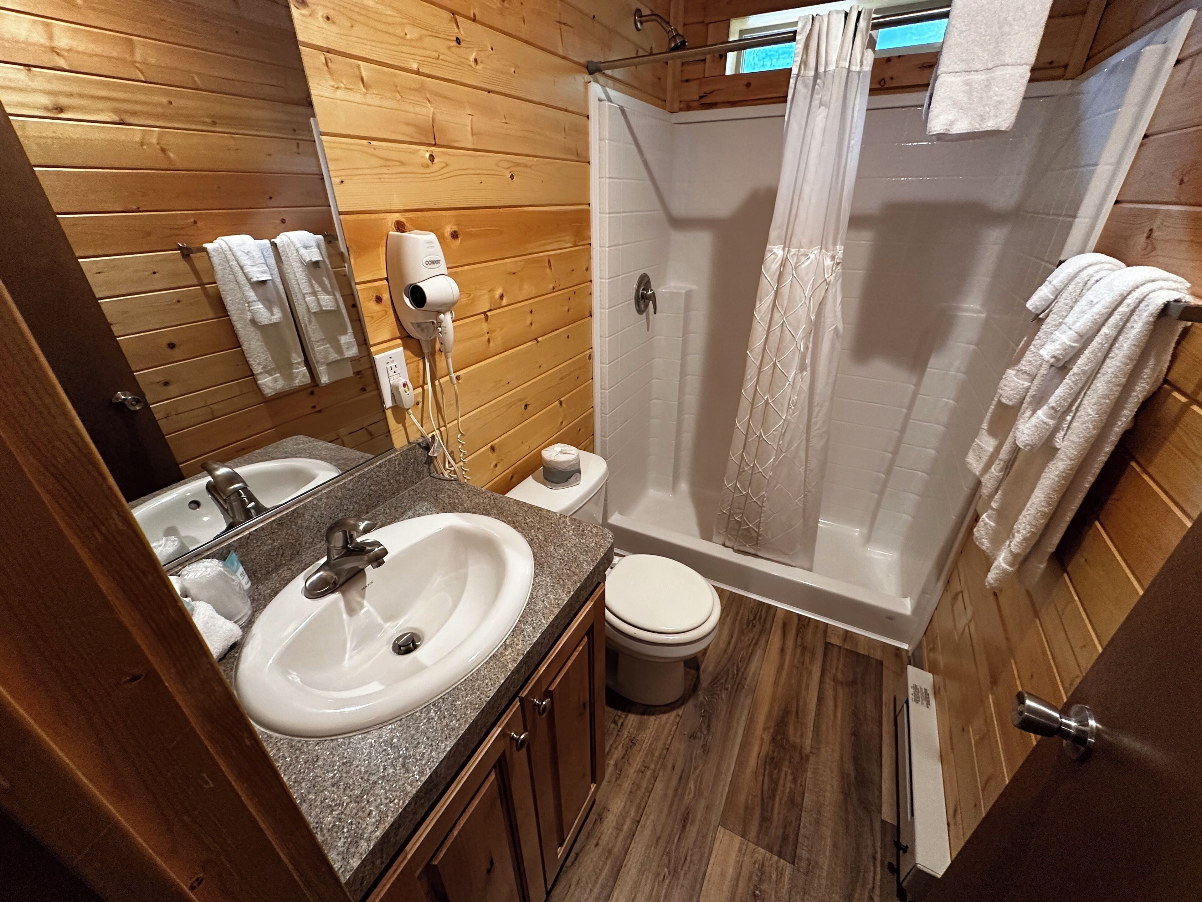 A wooden-paneled bathroom with a sink, toilet, and shower.