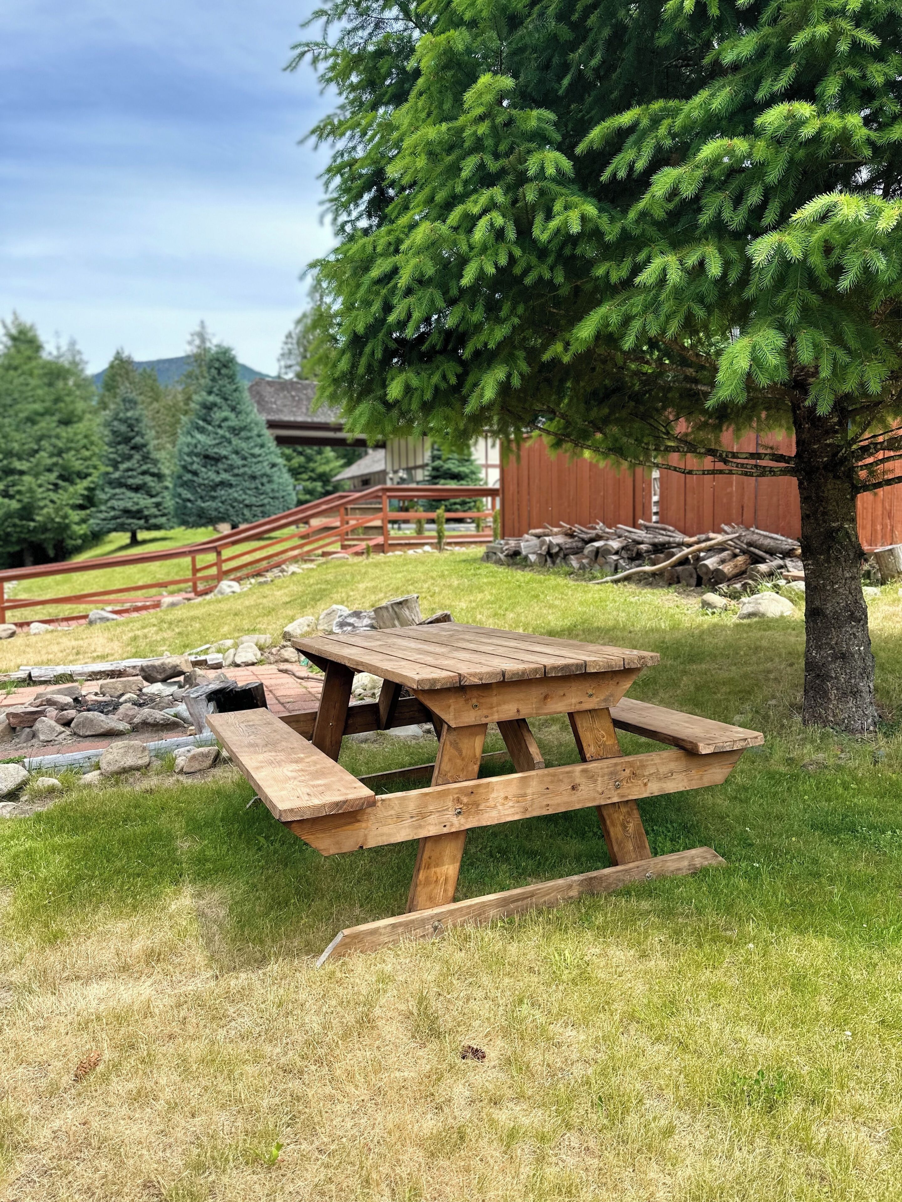 Une table de pique-nique se trouve dans un espace herbeux, avec une clôture en bois et des arbres en arrière-plan.