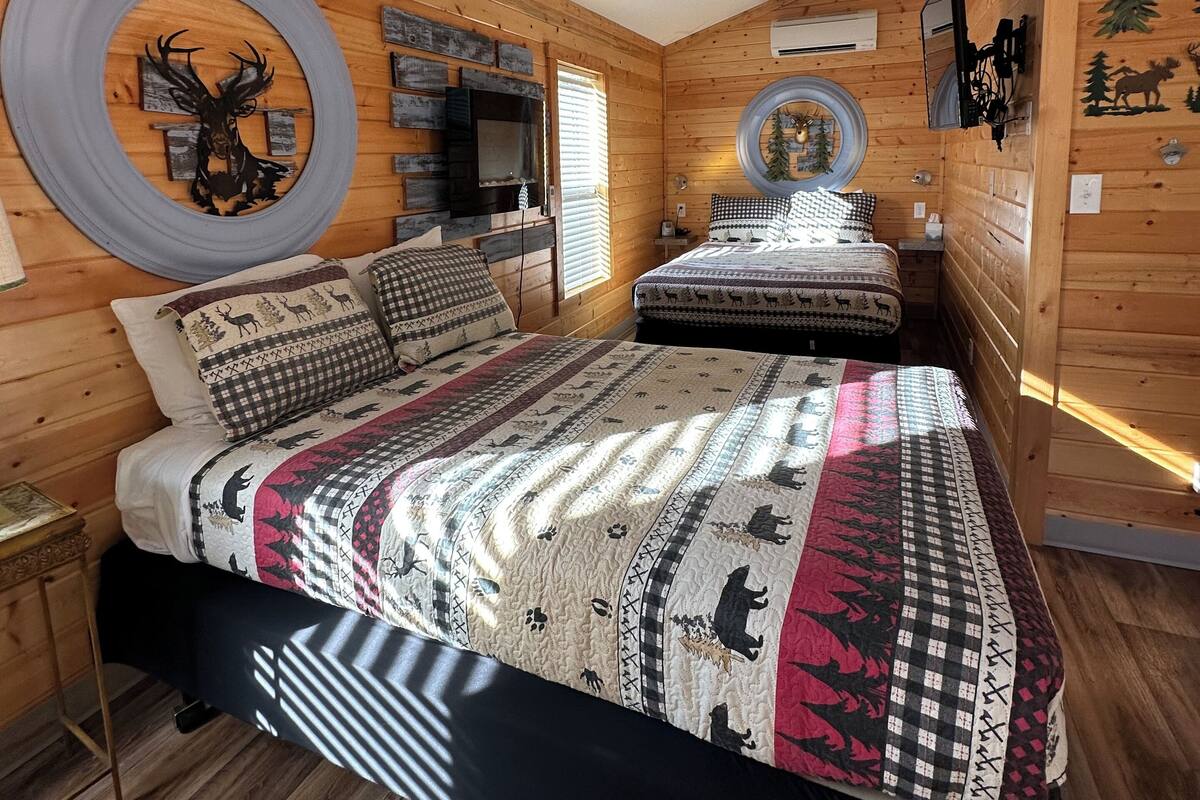 Ein gemütliches Schlafzimmer im Chalet-Stil mit einem großen Bett, einer runden Wanddekoration, einem Kamin und einem Fenster mit Blick ins Freie.