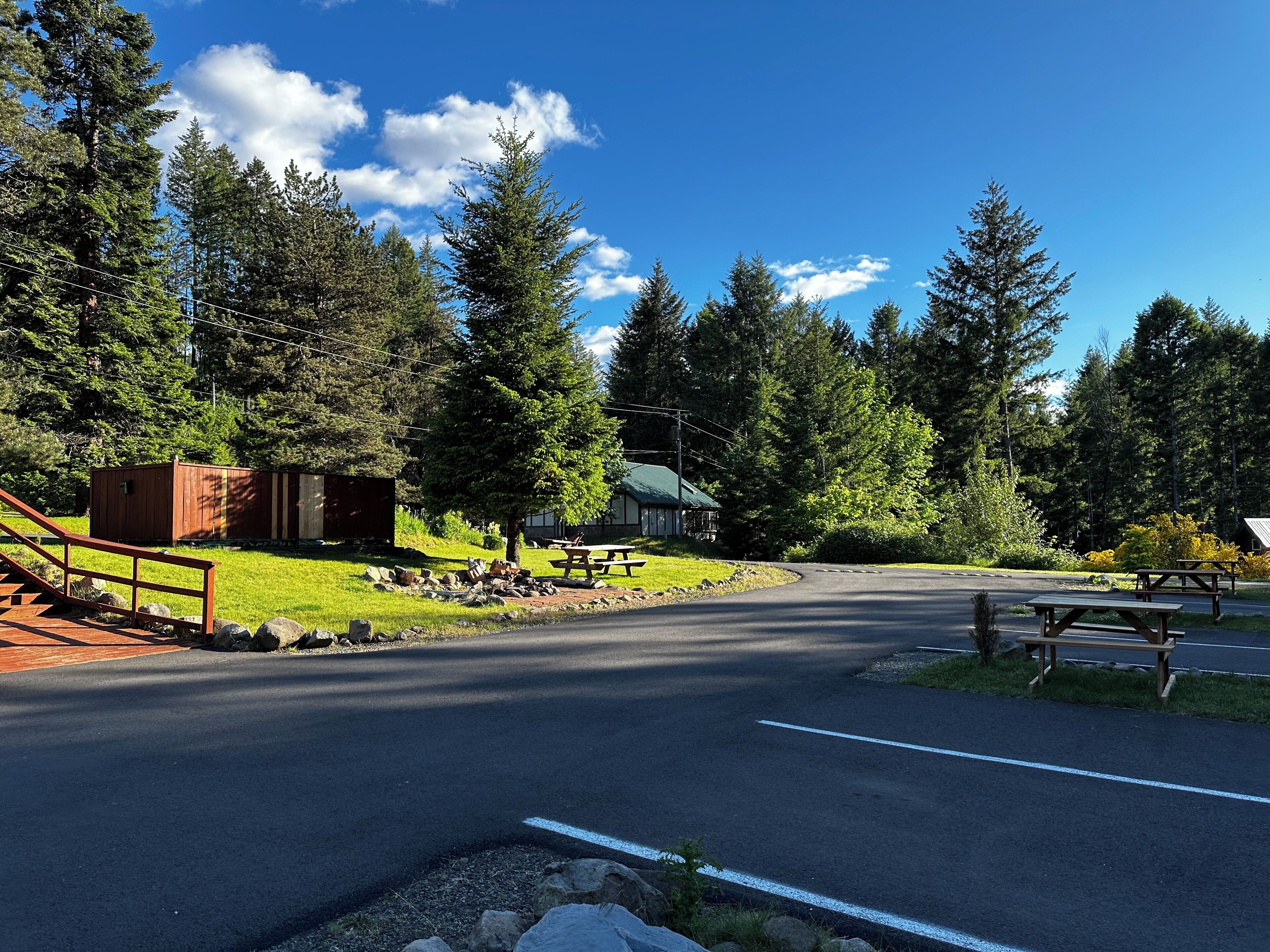 A road leading to a cabin with picnic tables and a small shed.