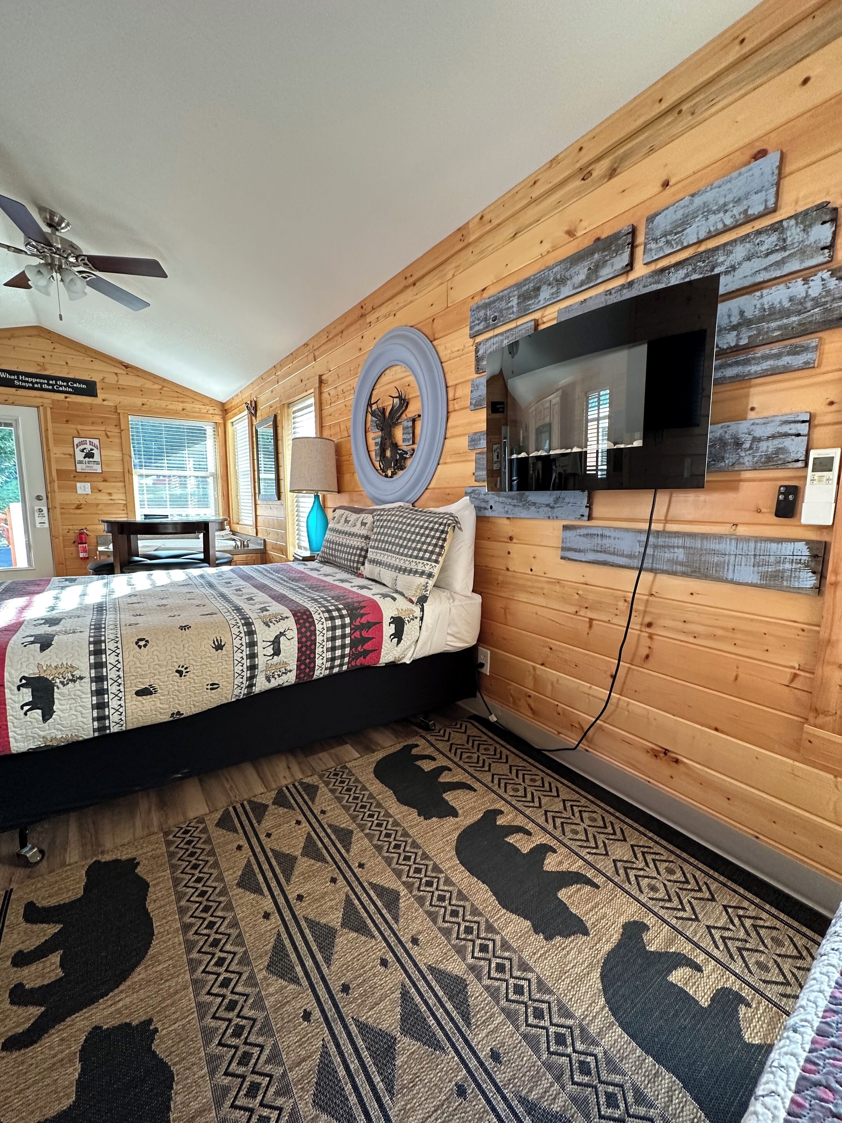 A cozy cabin-style room with a bed, a television mounted on the wall, and a ceiling fan.