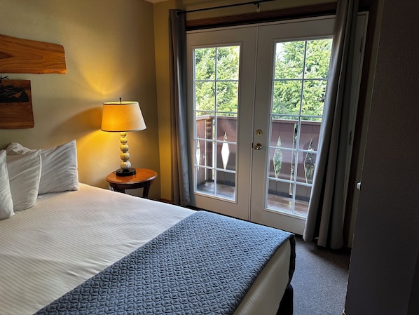 Habitación de hotel con cama, lámpara, vista por una puerta y un cuadro colgado en la pared.