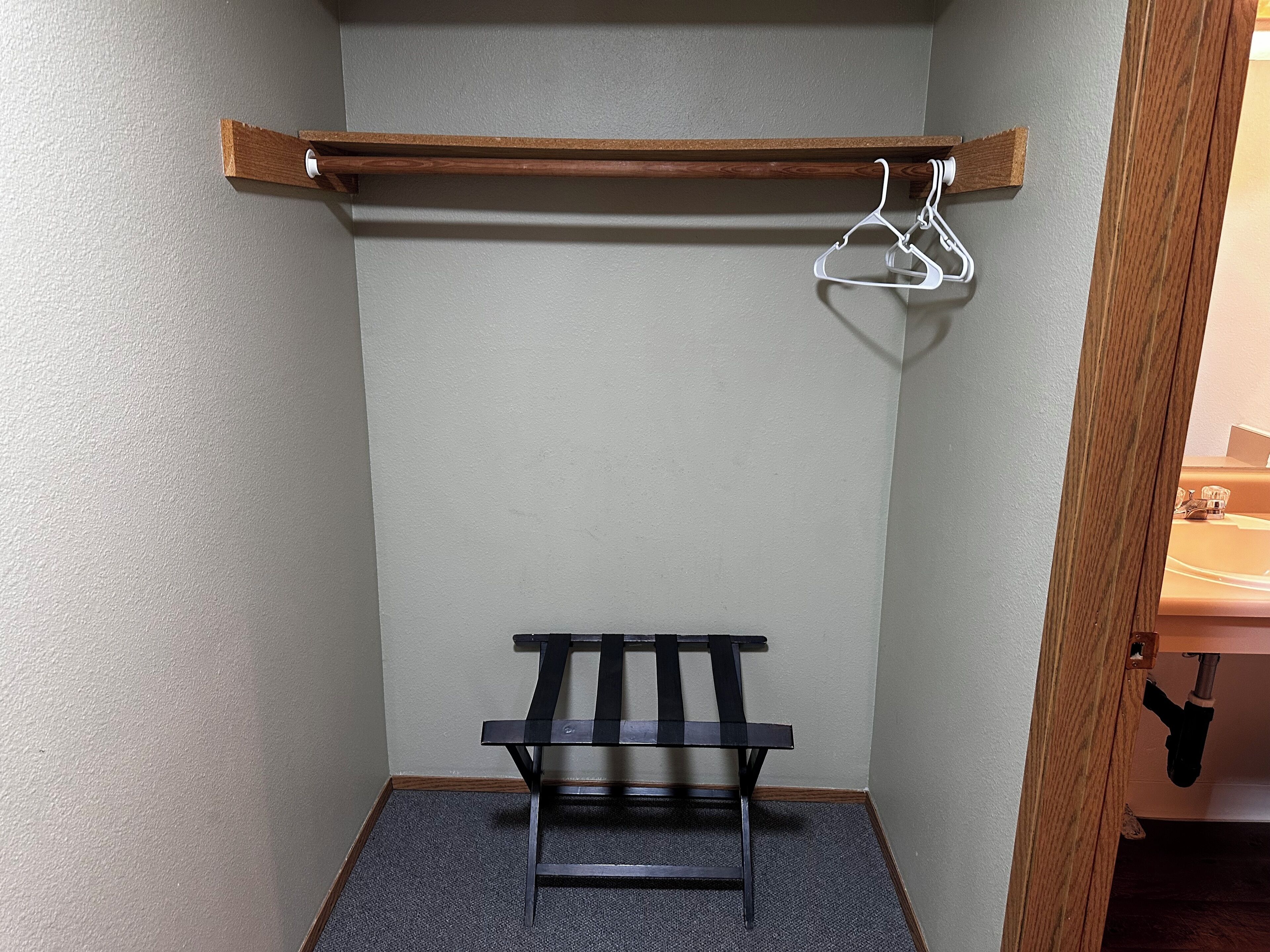 A small, enclosed room with a wooden shelf, a black bench, and a white hanger.