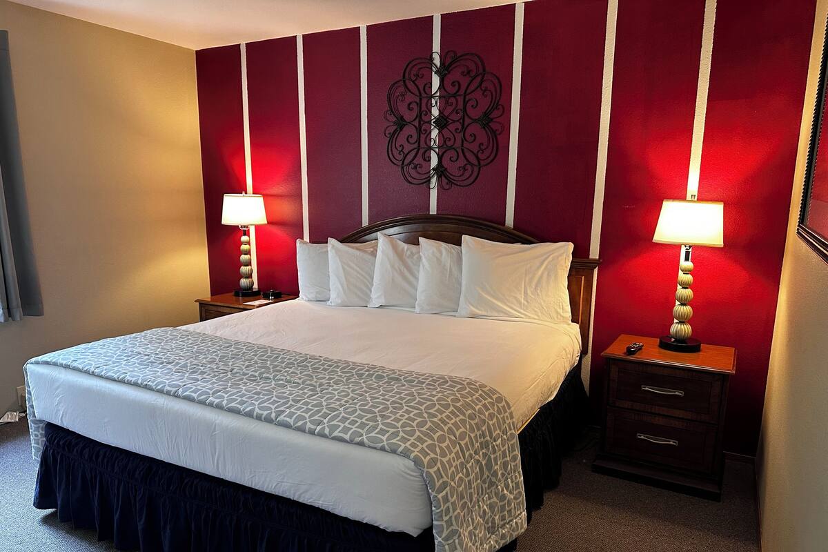 Ein Hotelzimmer mit einem großen Bett, zwei Nachttischen mit Lampen, einem Wandbild und einem Teppichboden.