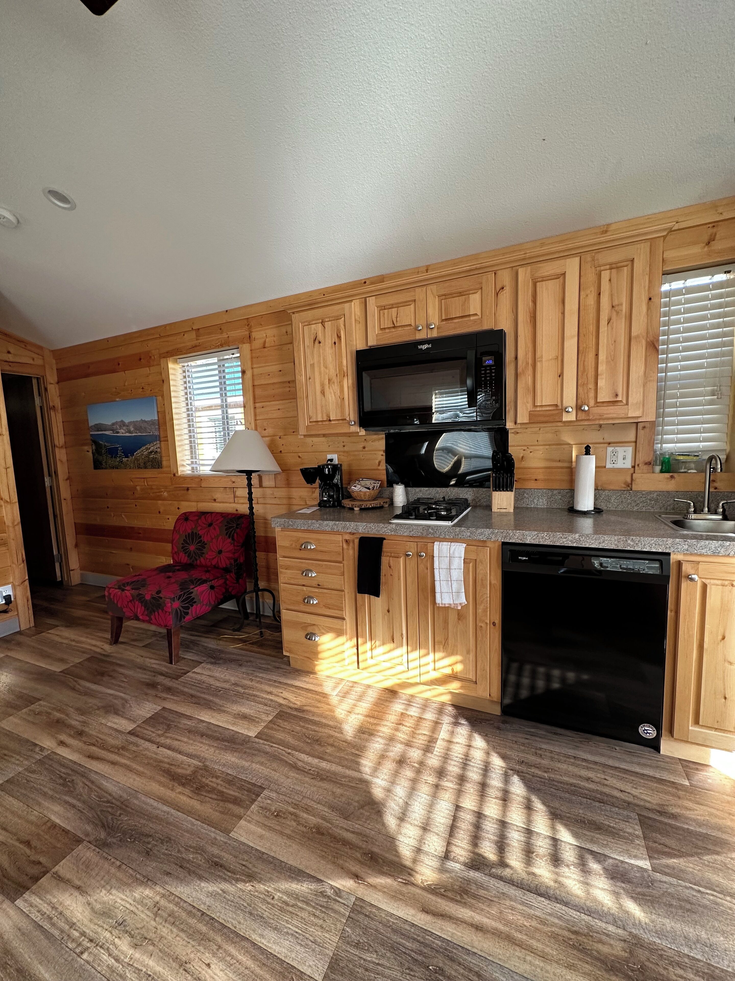 Una cocina con armarios de madera, microondas, lavavajillas y una silla.