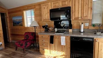 Una cocina con armarios de madera, microondas, lavavajillas y una silla.