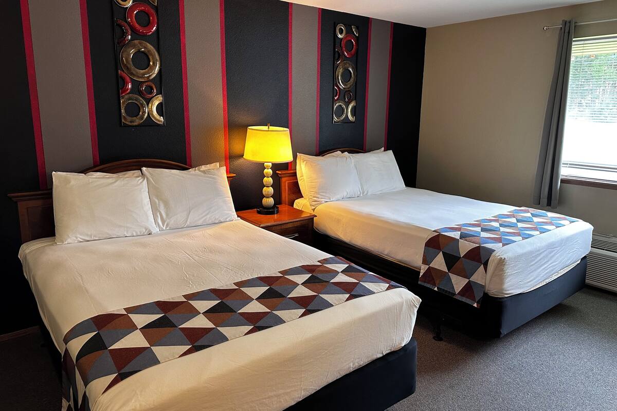 Ein Hotelzimmer mit zwei Betten, einem Nachttisch mit Lampe und dekorativen Wandbildern.