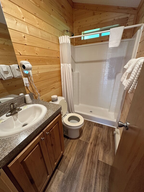 A compact bathroom with a wooden interior, a sink, toilet, and a shower stall.