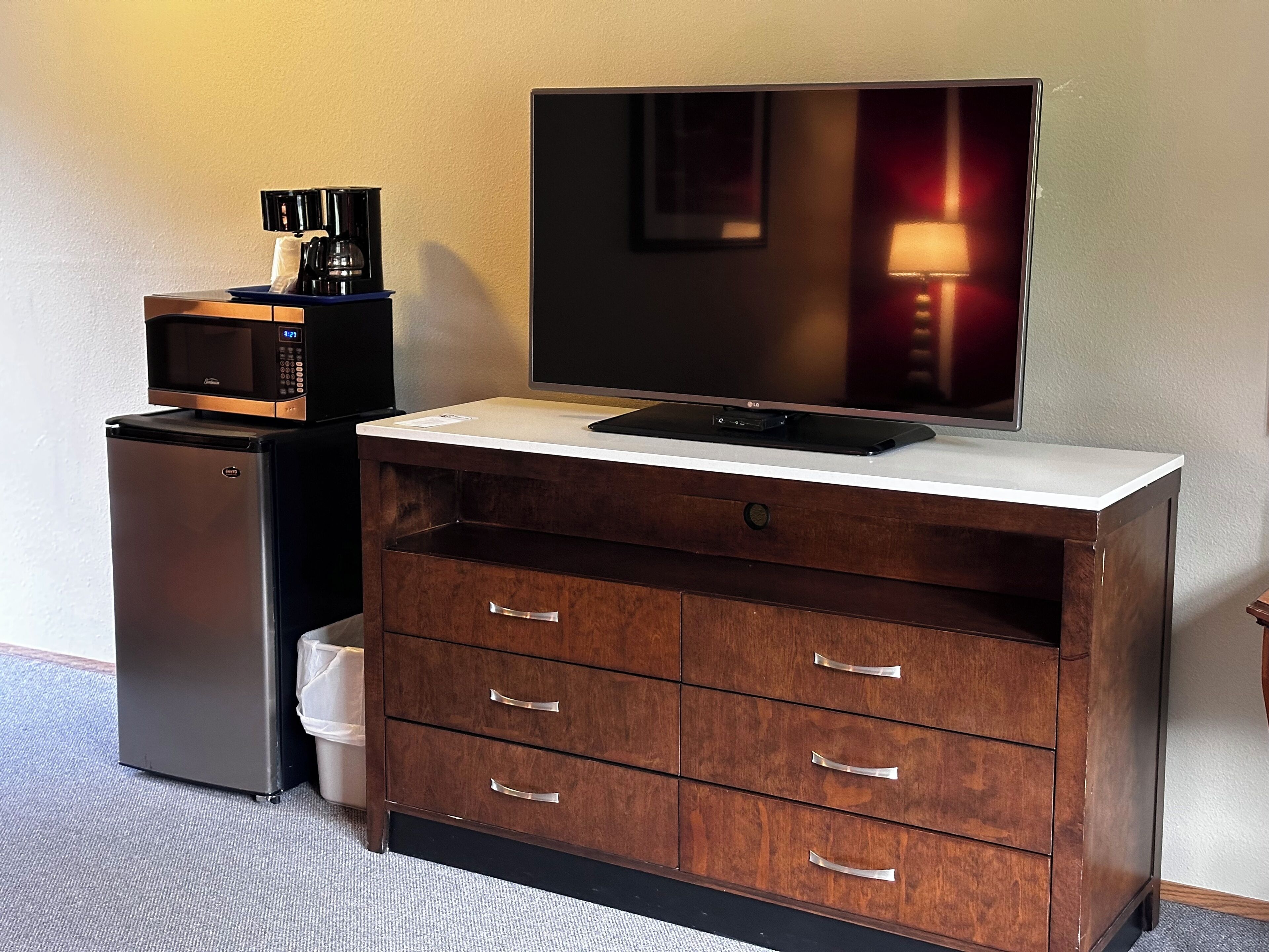 A compact kitchenette with a microwave, coffee maker, refrigerator, and a flat-screen TV on a wooden cabinet.