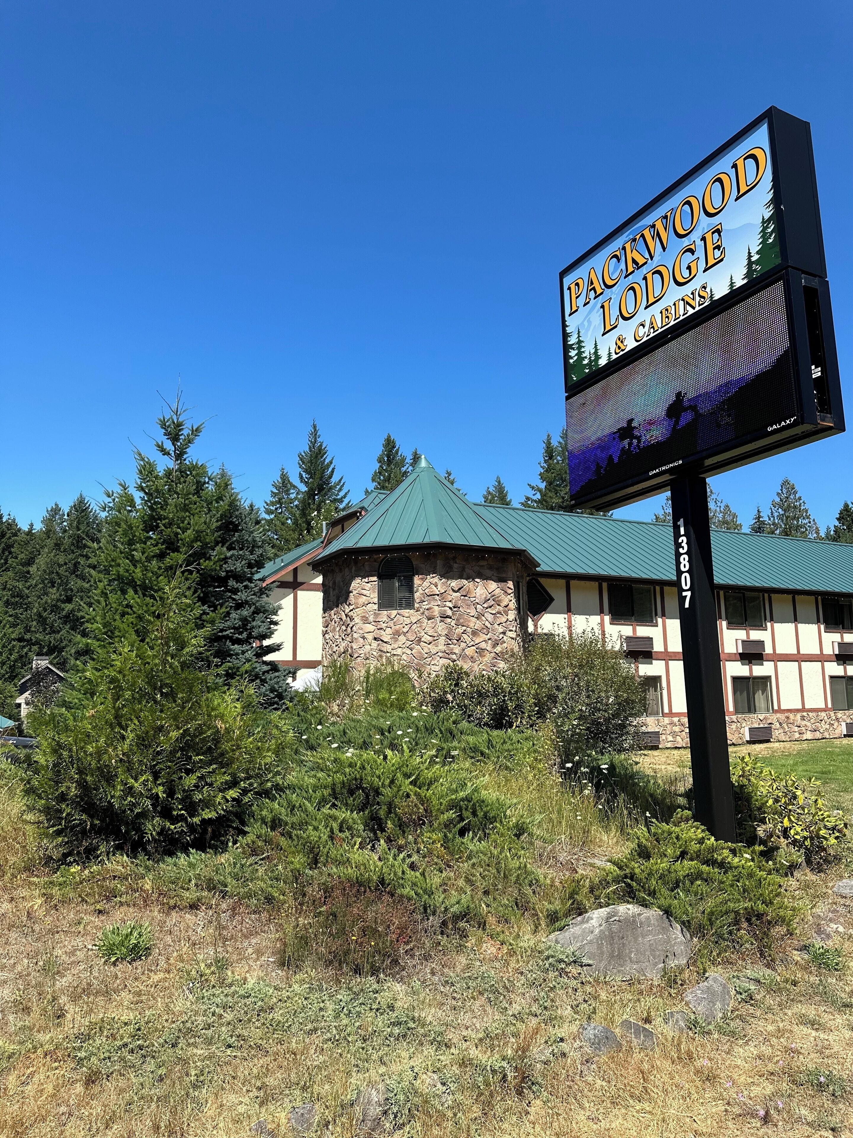 A sign for Packwood Lodge & Cabins with a stone building and green roof.