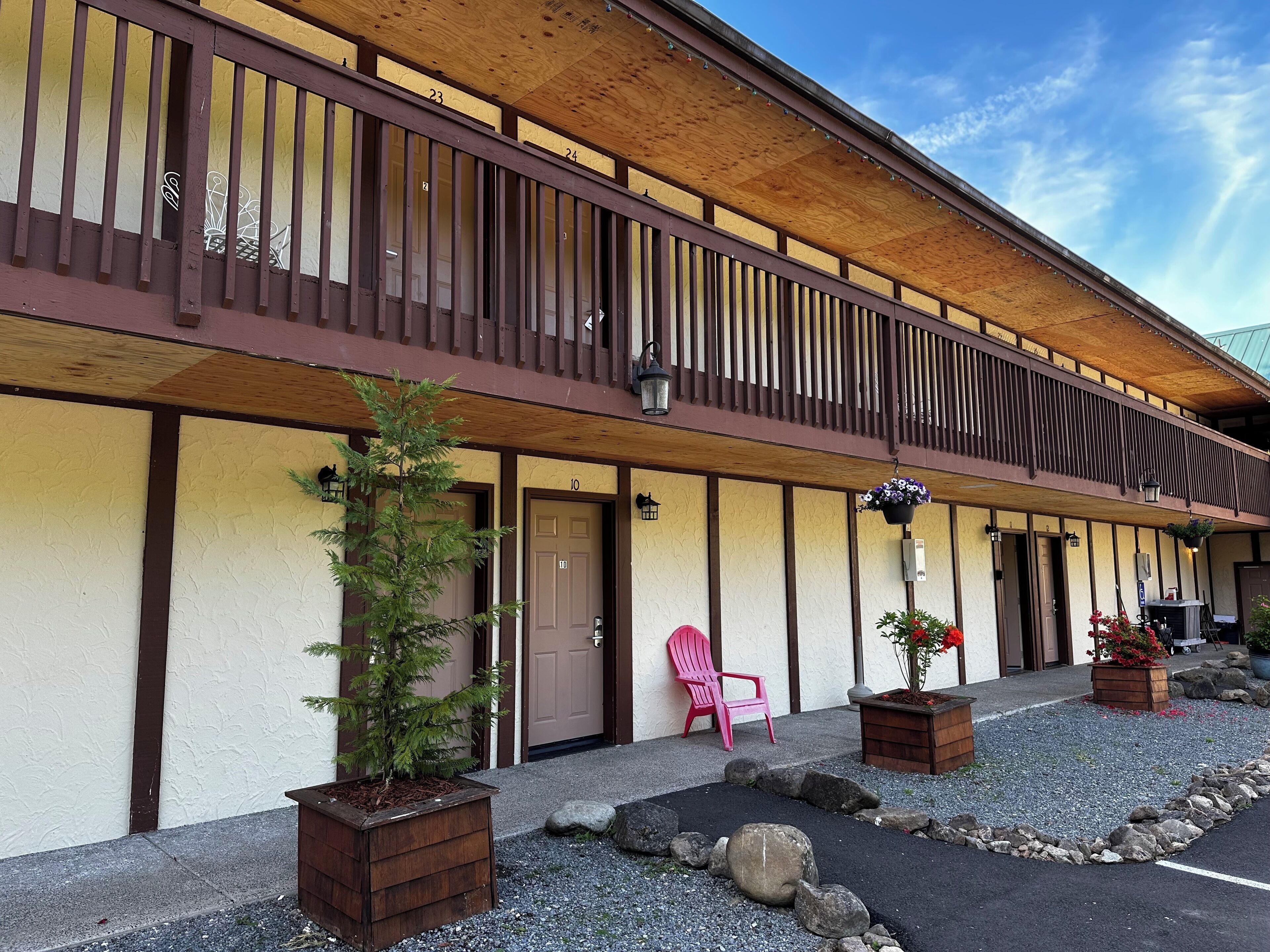 A two-story building with a wooden balcony, numbered doors, and outdoor seating.