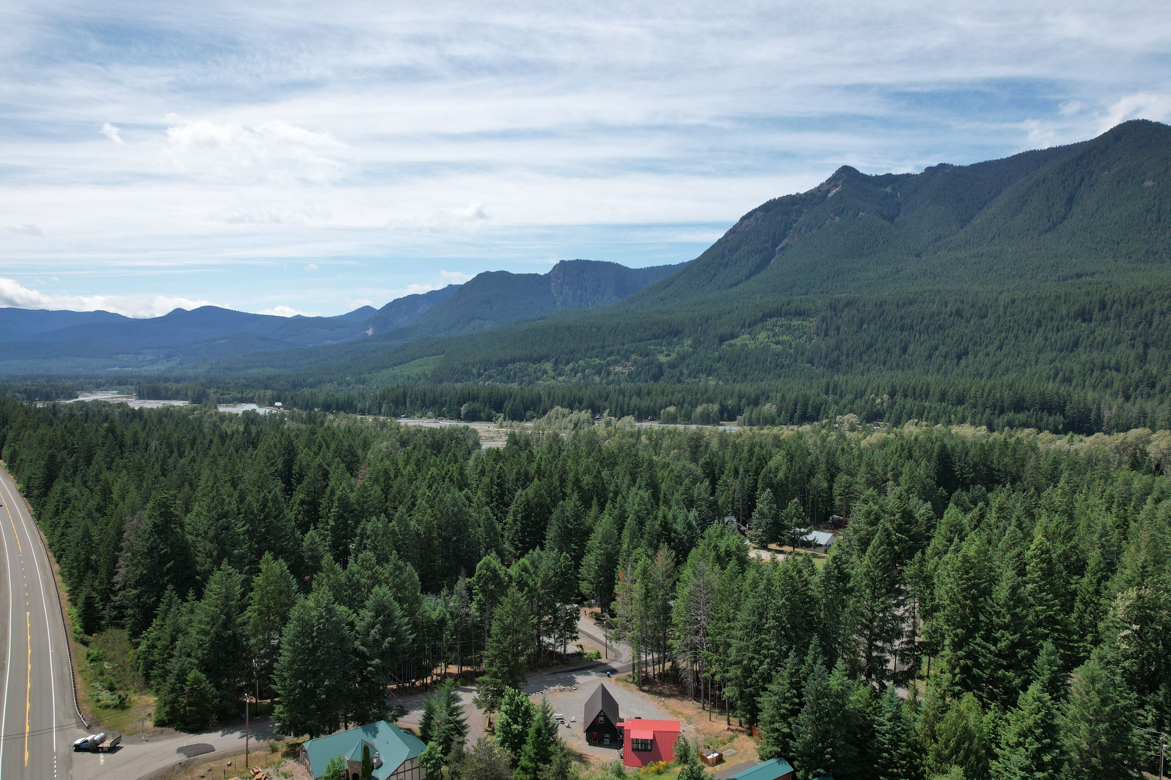 A forested mountain area with a road, a small building, and a red-roofed structure.