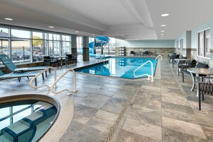 Zona de piscina de hotel con jacuzzi, sillones de descanso y un tobogán.