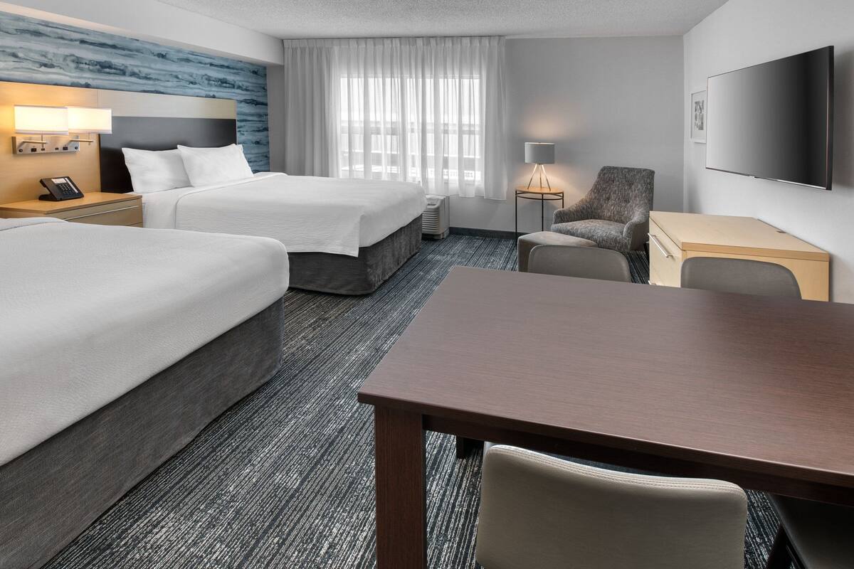 Une chambre d’hôtel avec deux lits, un bureau, une chaise, une télévision et une fenêtre avec des rideaux.