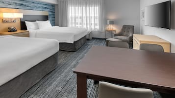A hotel room with two beds, a desk, a chair, a TV, and a window with curtains.
